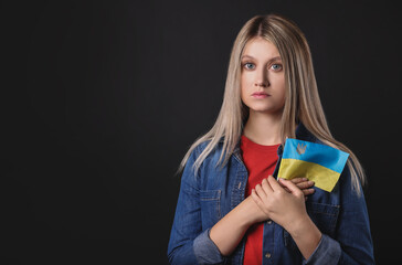 Wall Mural - Sad woman holding Ukrainian flag on black background. Space for text