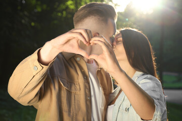 Poster - Affectionate young couple kissing and making heart with hands in park