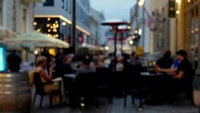 Defocused View Of Cozy Outdoor Restaurant At Evening. Unidentified People Eating Food And Having Conversation In An Outdoor Restaurant. Blurred Real Time Scene. People Having Fun And Drinking Wine.