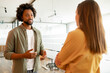 © Vadim Pastuh - Two coworkers chatting during coffee break standing in glass hall of office building. Curly african-american male employee explain something for female colleague, sharing his ideas