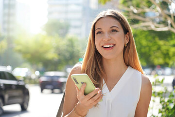 Wall Mural - Brazilian confident businesswoman looking away holding smartphone outdoors on summer