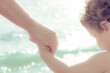 Detail of child holding grandfather hand on the beach near the sea