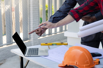 Wall Mural - Engineers and architects pointing at laptop screens looking at blueprints. Two Construction Engineers or Architects discussing at work with laptop on construction site and pointing on laptop.