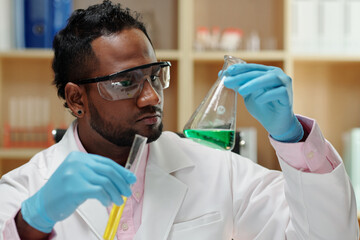 Wall Mural - Serious researcher looking at flask and test-tube with green and yellow liquids