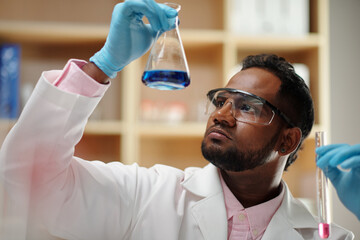 Wall Mural - Serious researcher looking at flask with blue liquid