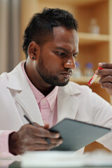 Wall Mural - Portrait of pensive scientist checking information on tubes with blood samples and writing data in document on tablet