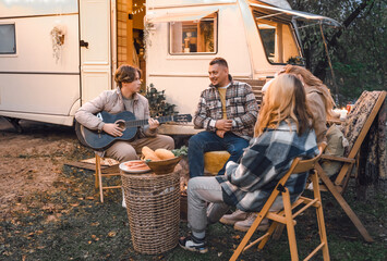 Wall Mural - Family trailer travel.Children,brother sister,mom dad playing guitar,singing song at fire.Evening picnic in nature.Holiday barbecue BBQ food.Vacation weekend dinner.Road lunch.Camper,house on wheels