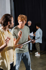 young actors with clipboards grimacing and showing okay signs during rehearsal in acting school.