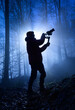 © Smileus - Silhouette of a videographer in a misty forest, dramatically backlit with cool blue color and rays of light behind him