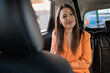 © Cristina - woman inside the back of a car, transport by cab , young girl talking to cab driver smiling. Person traveling for work, dressed in orange blazer and cream sweater. Very pretty and natural girl.