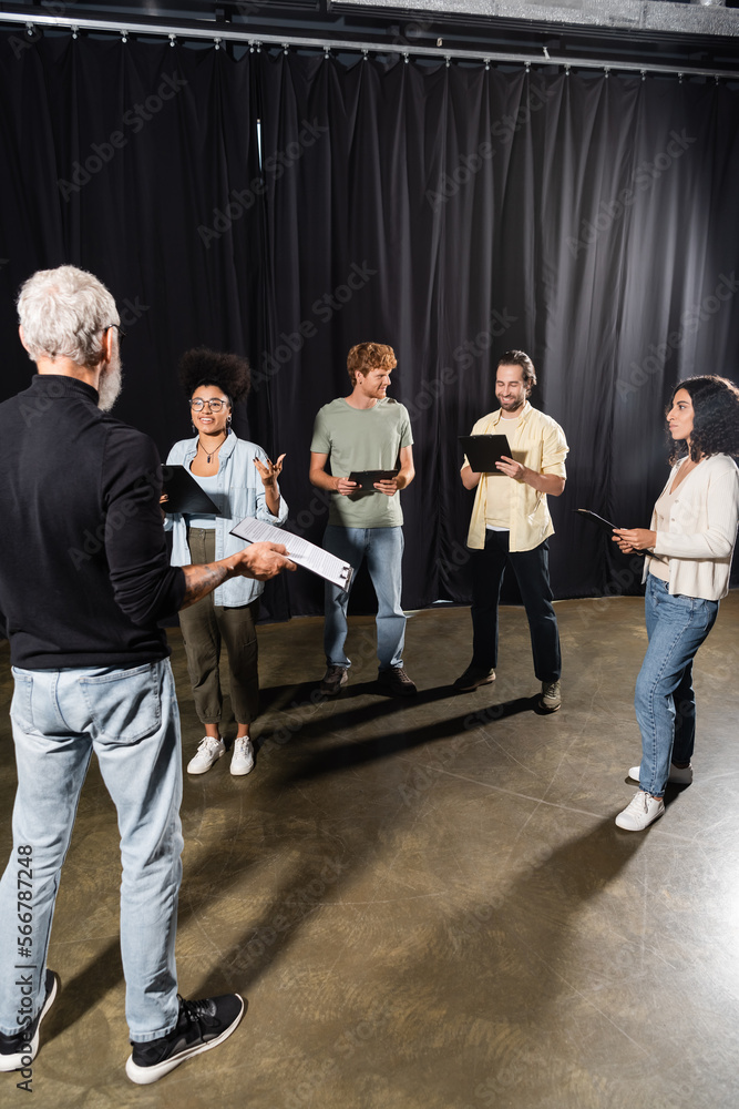 multiethnic actors standing with screenplays near grey haired art ...