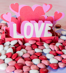 Valentine's day greeting card with red chocolate hearts around it on a pink marble table. The party of the lovers