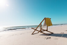 Empty Deckchair With Yellow Napkin On Sandy Beach Under Clear Blue Sky During Sunny Day