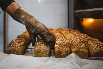 Baker man sorting seed loaves with an oven mitt in a bakery