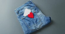Close Up Of Folded Jeans With Heart And White Note On Grey Background With Copy Space
