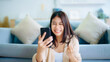 © Monster Ztudio - Happy young asian woman relax on comfortable couch at home texting messaging on smartphone, smiling girl use cellphone, chatting online message, shopping online from home