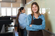 © amorn - Smiling young woman working at coffee shop. Happy female waitress or cashier working in the coffee shop