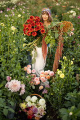 Portrait of a woman with lots of freshly picked up colorful dahlias and lush amaranth flower on rural farm during sunset