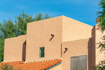 Block style building with adobe design or architecture with flat roof and tiny red tiles and back or front yard trees in sun