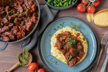 Wall Mural - Italian pork ragout with creamy polenta and green beans on wooden table for dinner or lunch. Flat lay