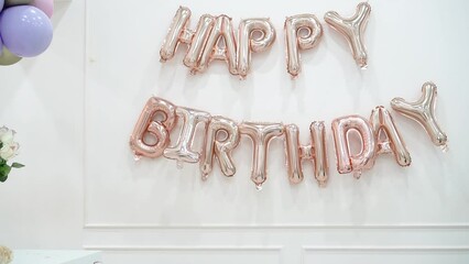 Wall Mural - A girl of 6 years old in a black dress jumps merrily against the background of the inscription in gold letters happy birthday above her head.