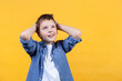 Portrait of a boy on a yellow background. He’s holding his head thinking. He’s looking up. Front view. Copy space.