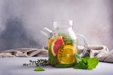 Wall Mural - Glass teapot of hot healthy fruit tea with fresh ripe citrus, mint and  thyme