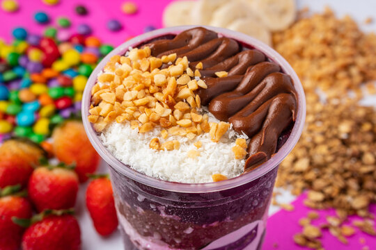 close up of acai or açaí cup with topping chocolate and nuts in colorful background