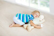 © famveldman - Baby sleeping on floor with toy and milk bottle.