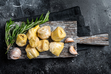 Wall Mural - Artichokes hearts marinated with olive oil and herbs, pickled artichoke with garlic on wooden board. Black background. Top view