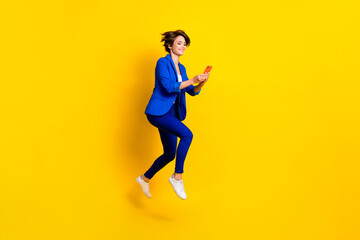 Sticker - Full length photo of good mood woman wear blue jacket typing samsung apple device jumping high isolated yellow color background