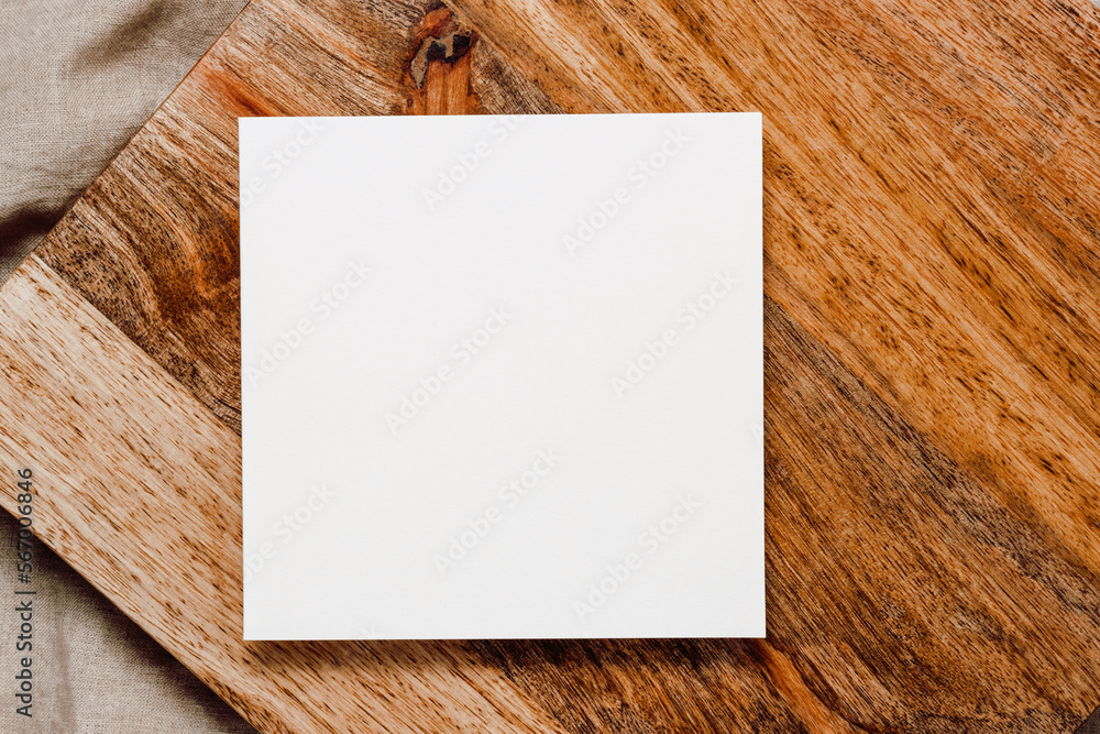 Blank paper sheet mockup card on wooden stand on linen beige cloth. Paper sheet card for invitation, social media, business branding and blog template, aesthetic minimal style. Top view, flat lay
