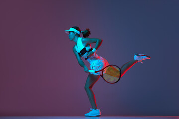 Portrait of young professional female tennis player in sports uniform in motion, action over gradient pink-purple background in neon light. Sport, fashion, energy, motivation concept