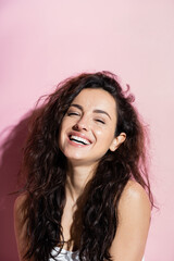 Wall Mural - Positive young woman with curly hair looking at camera on pink background.