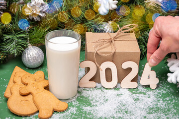 Cookies, a glass of milk for Santa on a table covered with snow on the background of Christmas decorations and gifts