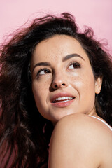 Wall Mural - Portrait of curly and freckled woman looking away on pink background.