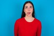 © Jihan - young brunette girl wearing red T-shirt against blue wall showing grimace face crossing eyes and showing tongue. Being funny and crazy