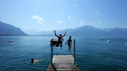 Wall Mural - People jumping into lake water. Father and son running in Swiss pier and diving into Geneva lake landmark. Parent and teen kid enjoying holidays