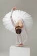 ballet dancer in white ballet tutu bowing on pedestal, isolated on gray studio background