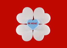 Be Mine Text On Blue Heart Sitting On Four White Foam Hearts On Red Background.