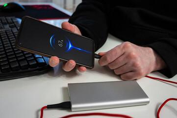 Male hands holding cellphone connected to a power bank