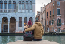 Young Couple Hugging In Winter In Front Of A Canal In Venice, On Honeymoon.