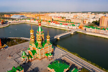 Summer Aerial View Of Golden-domed Orthodox Cathedral Of Annunciation Of Blessed Virgin, Pedestrian Bridge Across Malaya Kokshaga River And Colorful Bruges Embankment In Yoshkar-Ola, Mari El, Russia