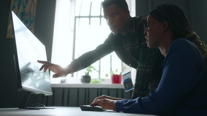 black woman designer and male engineer discussing project in office, looking at display of computer