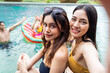 © Kawee - Asian women friend in bikini use mobile phone taking a photo at a pool.