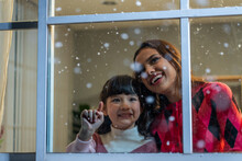 Adorable Child Looking At The Window And Admire Snowflakes With Mother.