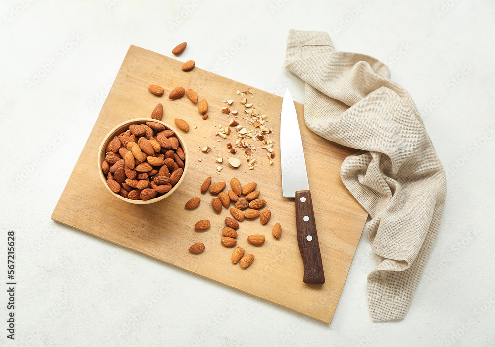 Wooden board with almond nuts and knife on light background