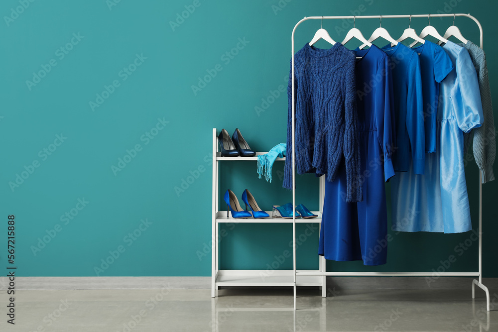 Rack with blue clothes and shoe stand near color wall