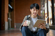 Smart young Asian male college student sitting on stairs outside and reading a book.