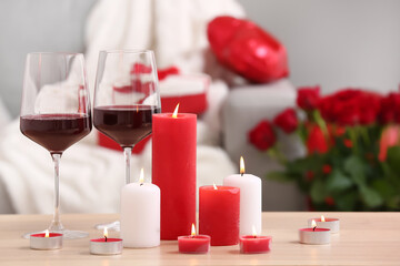 Burning candles and glasses of wine for Valentine's Day on table in living room, closeup